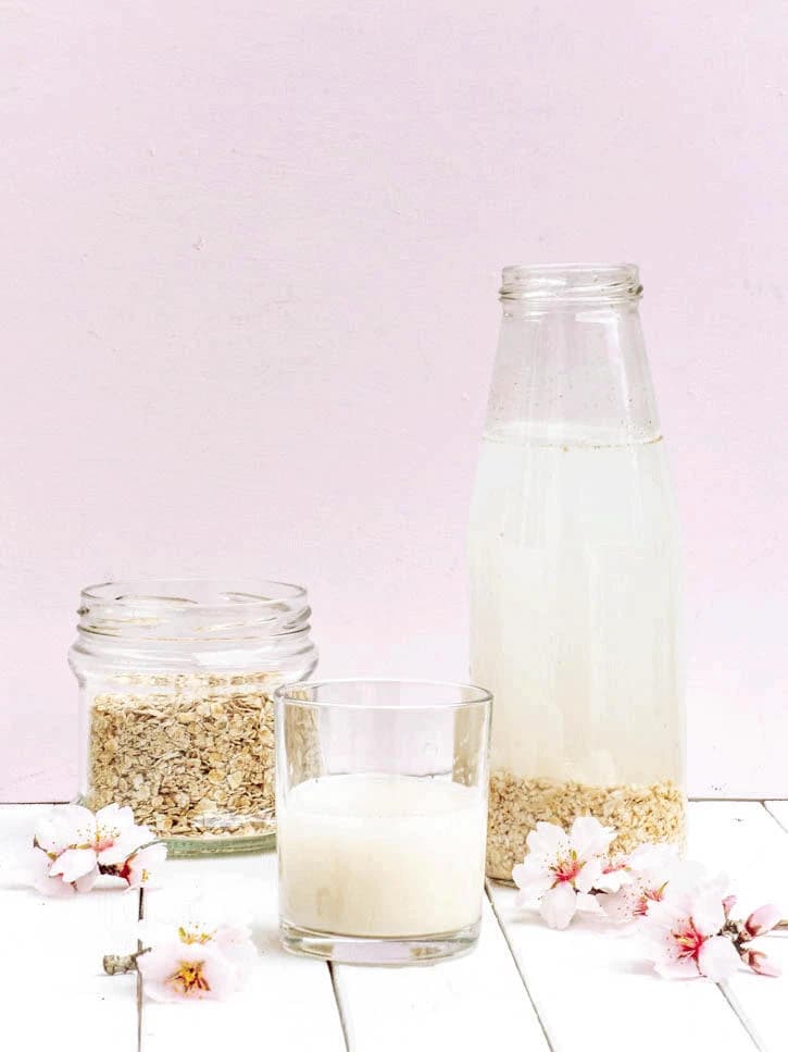 Verre de lait d'avoine maison, accompagné d'un pot de flocons d'avoine et d'une bouteille en verre