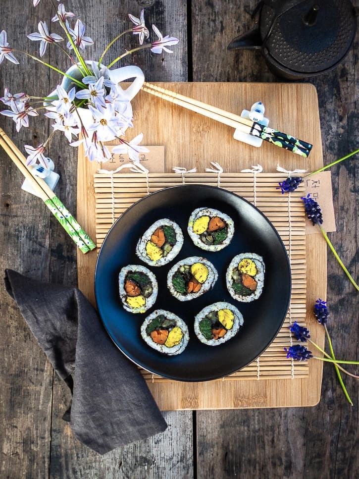 Kimbap vegan coupés en tranches sur une assiette noire présentée sur un tapis de bambou