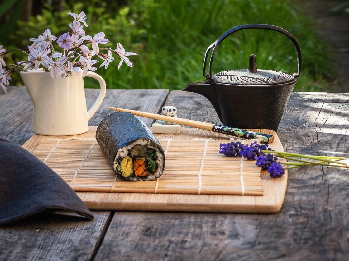 Rouleau de kimbap végétalien vu de face sur une planche dans un décor de jardin