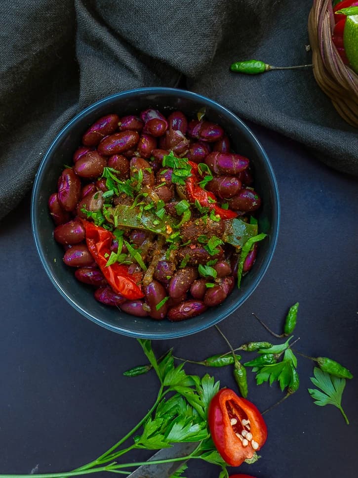 Bol de haricots rouges relevés de persil et de piment rouge, posé sur un linge sombre