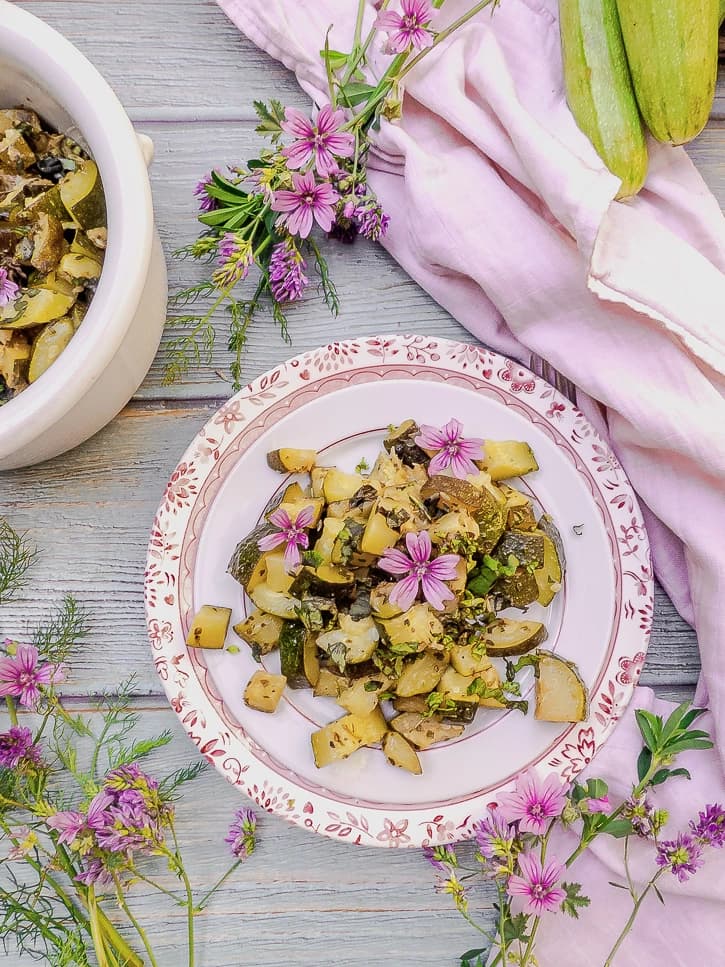 Assiette de salade de courgettes vegan sur fond gris bleu avec décor rose